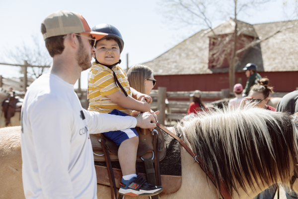 ranch day horseback ride a young child rides a buckskin horse, with an adult walking alongside them