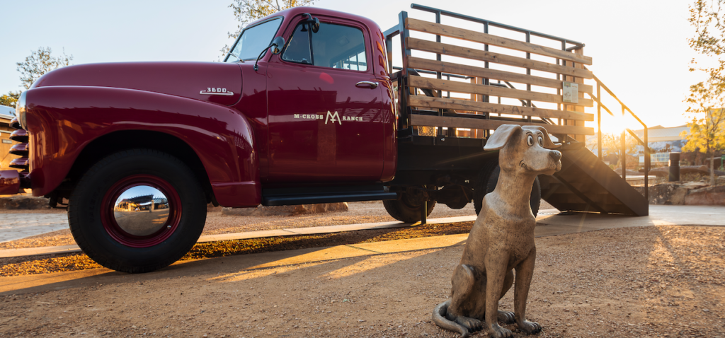 a statue of Hank the Cowdog stands in front of an old red ranch truck at the cash family ranch life learning center