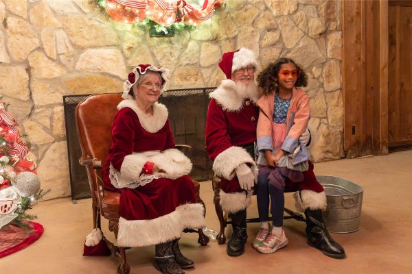 A young girl taking a photo with Santa and Mrs. Claus.