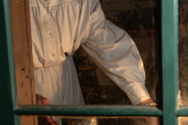 A woman sprinkles powdered sugar on fresh waffles by the window.