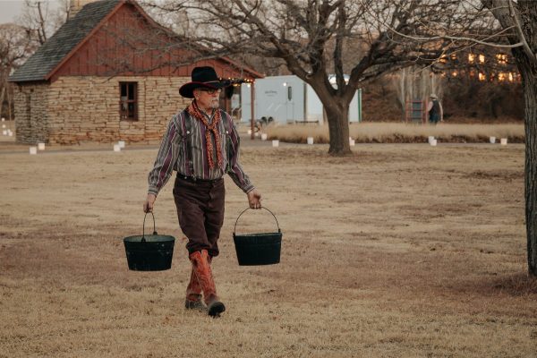 A cowboy carrying two buckets of water.