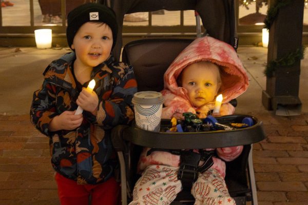 A young boy and young girl in a stroller hold up fake lit-up candles.