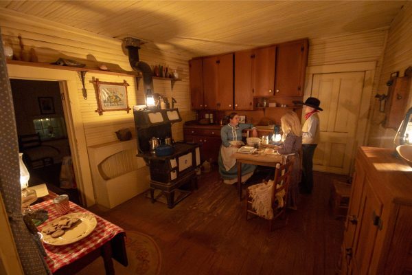 A mom, son and daughter make gingerbread by oil lamp inside the Harrell House.