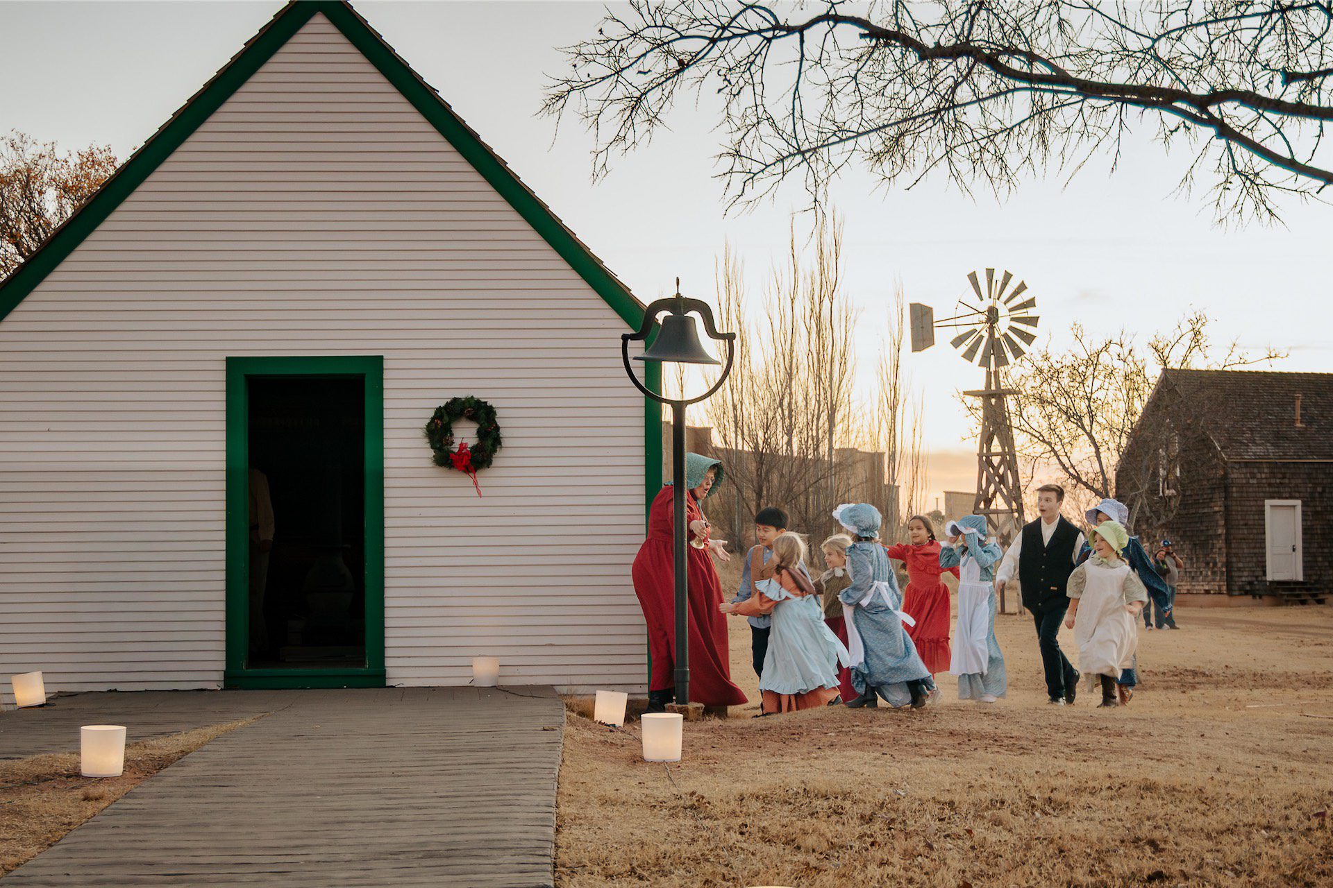 Children and teacher walking toward a one-room schoolhouse.