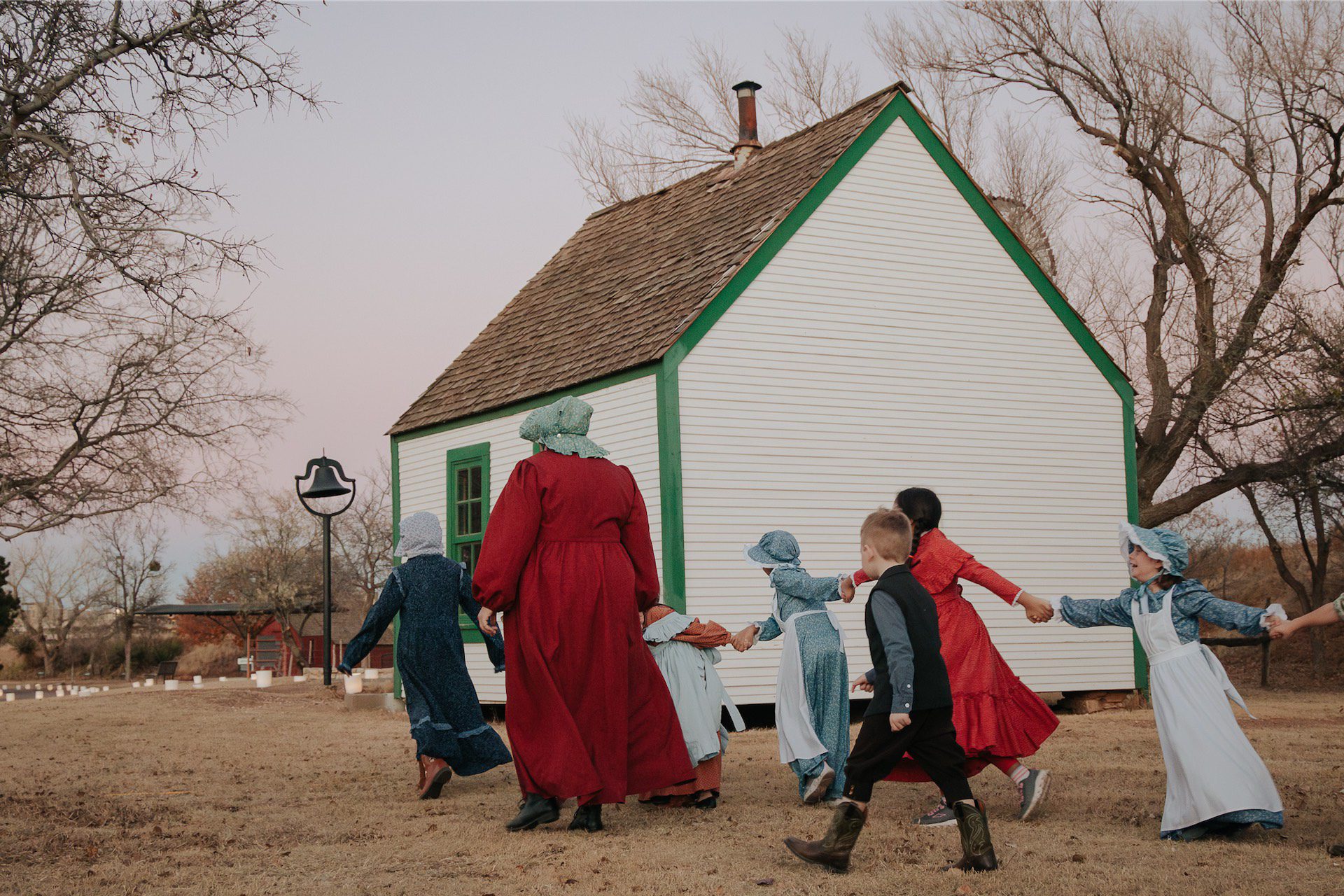 Children and teacher walking toward a one-room schoolhouse.